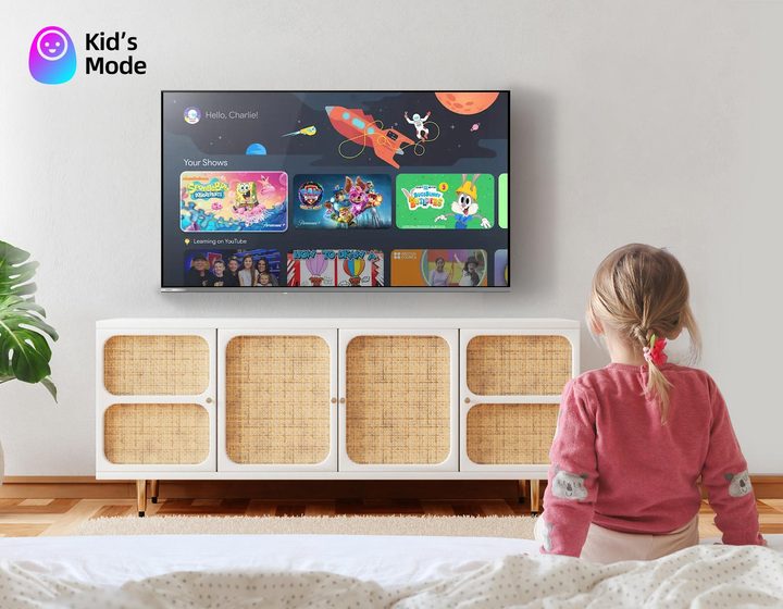 A small child sitting on a bed watching the Kids Mode home screen