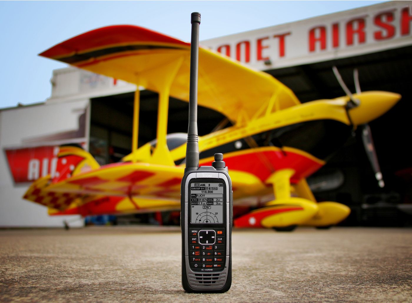 An iCOM air band handheld in front of a yellow biplane