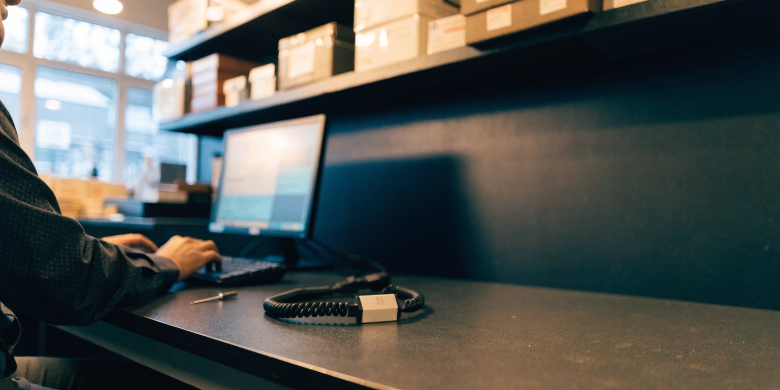 A technician at a service bench programming a radio at a computer, with an iCOM IC-41PRO handheld standing on the bench