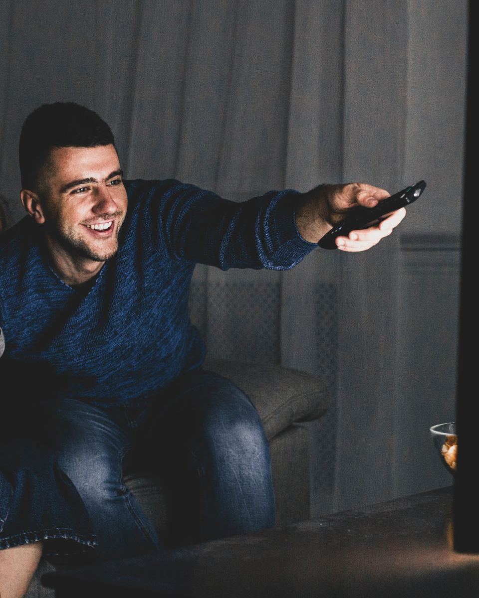 A man on the couch pointing the remote at the TV