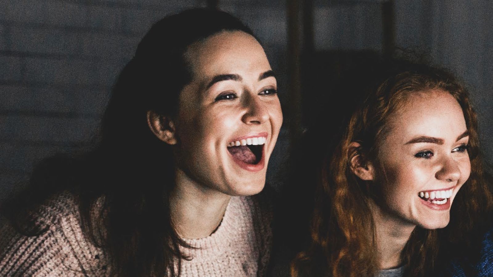 Two friends laughing on the couch during a movie night