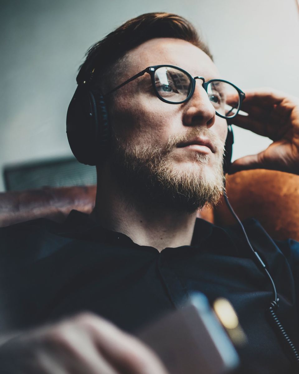 A man listening on headphones, lit by a window